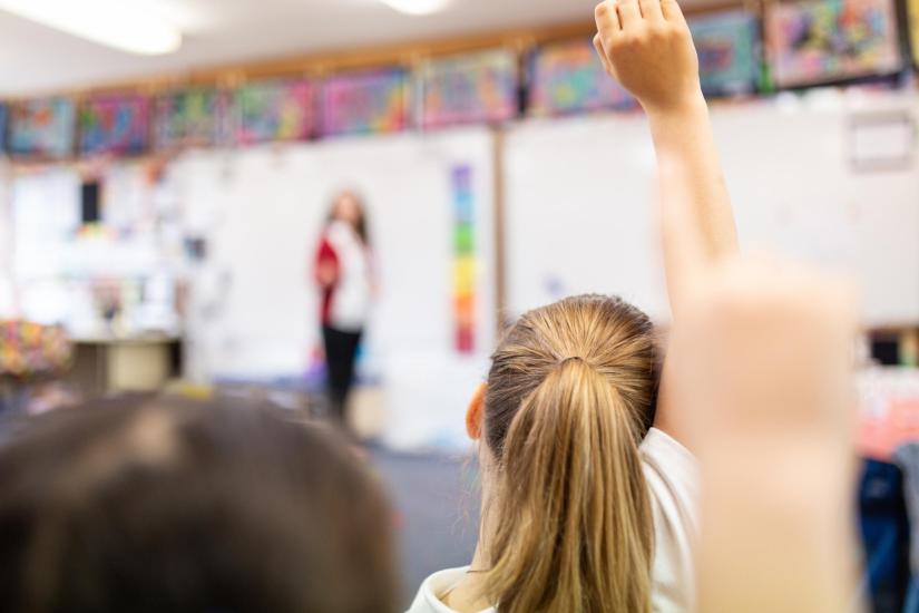 Children in classroom raising hands