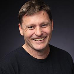 Man with short brown hair smiling and look at the camera in a black tshirt