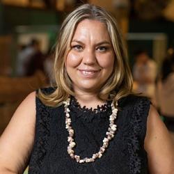 Indigenous woman with shoulder length hair in a black sleeveless dress and traditional necklace smiling and looking at the camera