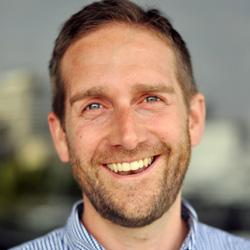 Man with short hair smiling and looking at the camera in a striped business shirt