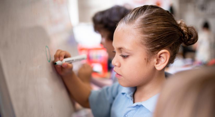 a child writes on a whiteboard in a classroom