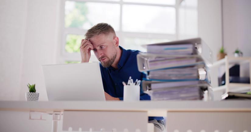 A man stares at a laptop in a home office, looking tired