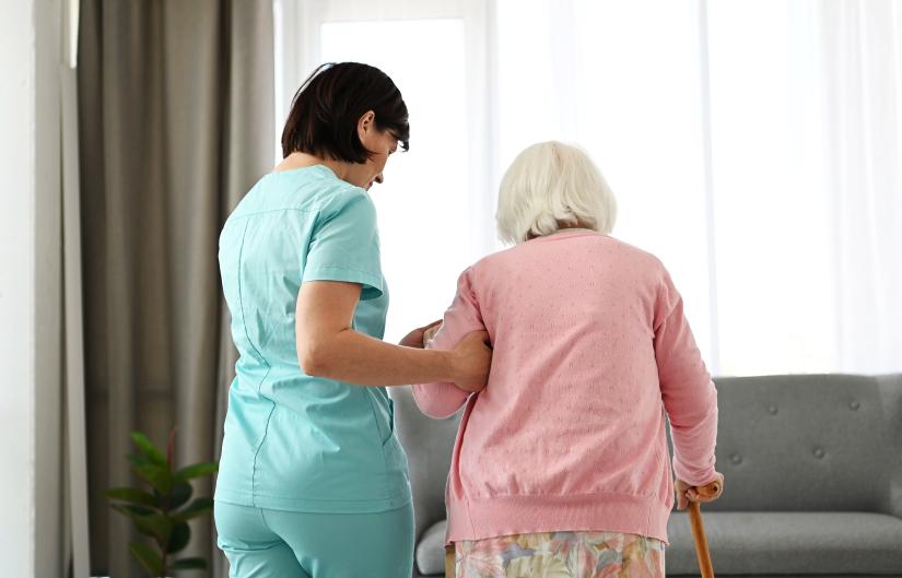 Stock picture: nurse helps an elderly woman walk around a room