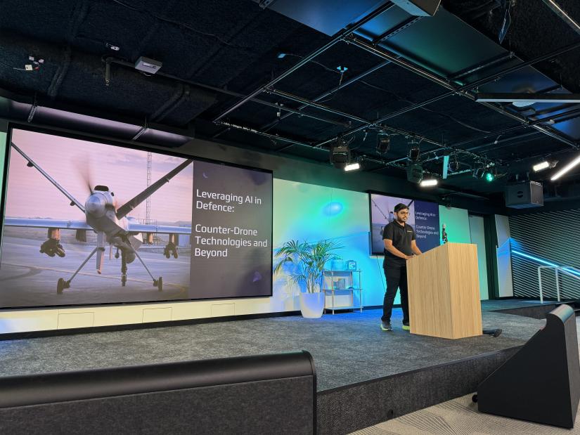 Man stands at podium in front of drone presentation.