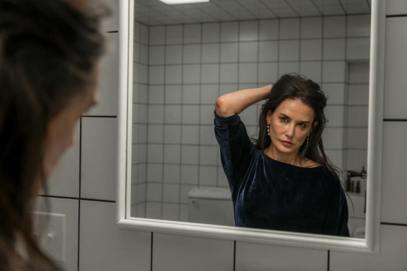 A publicity still for The Substance, actress Demi Moore looks at her reflection in a mirror