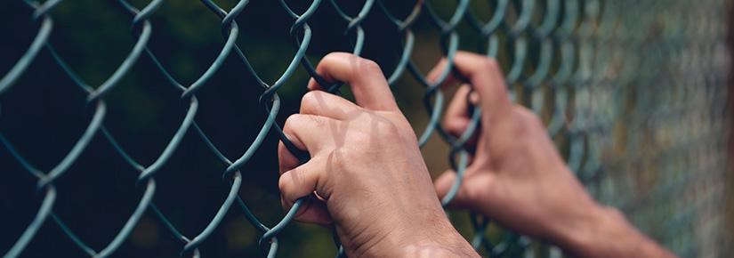 Young person's hand holding onto a chain link fence