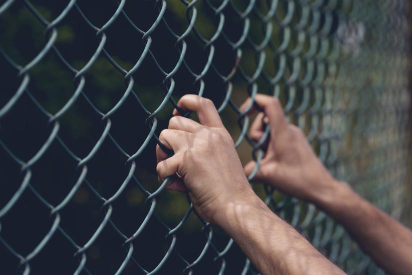 Young person's hand holding onto a chain link fence