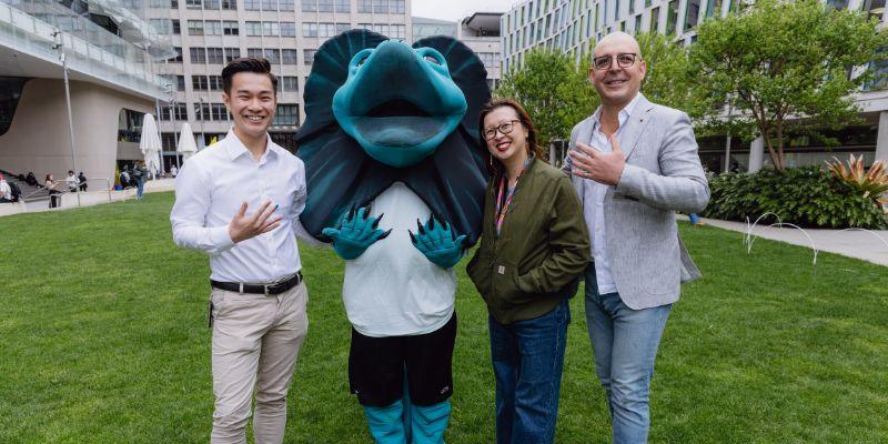 Three people and UTS mascot Lenny are standing outside, holding up their hand