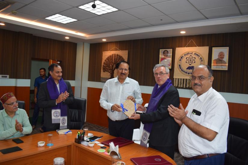 Two men wearing purple scarves are presented with a certificate.