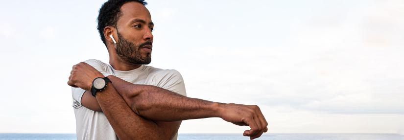 African American man stretching arm, warming up before workout and running session outdoors. Exercising near the ocean.