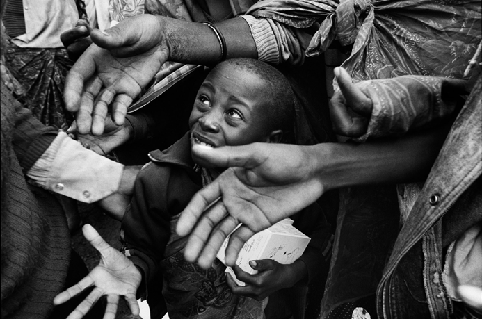 Black and white image of little Rwandan boy looking up from inside a crowd of adults
