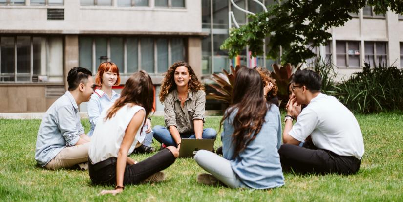 Group of diverse students sitting in a circle on the Alumni Green, smiling and chatting