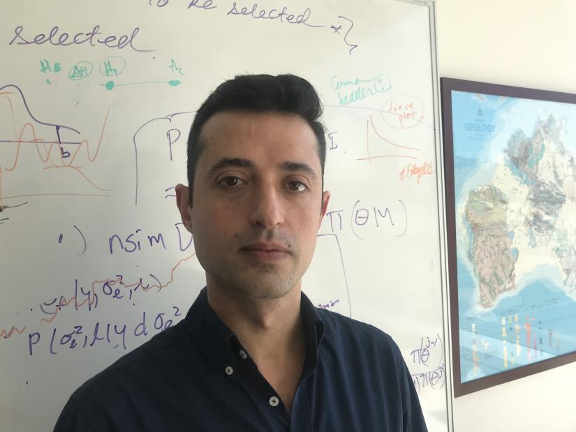 Man in dark shirt, standing in front of white board with formulas
