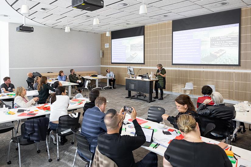 Interactive classroom at UTS with a UTS staff member at the front of the room speaking to groups of alumni sitting at tables.