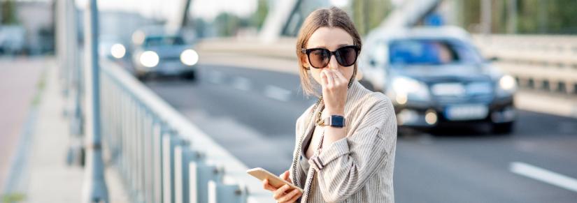 Woman closing her nose feeling bad because of the air pollution on the bridge with traffic in the city