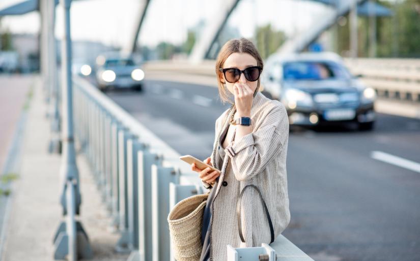 Woman closing her nose feeling bad because of the air pollution on the bridge with traffic in the city