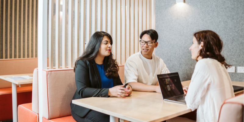 Three student sitting a table and talking. A laptop is on the table in front of one student