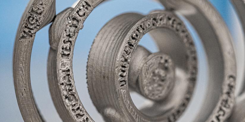 Close up of sintered metal 3D printed part of a multibody medallion featuring text