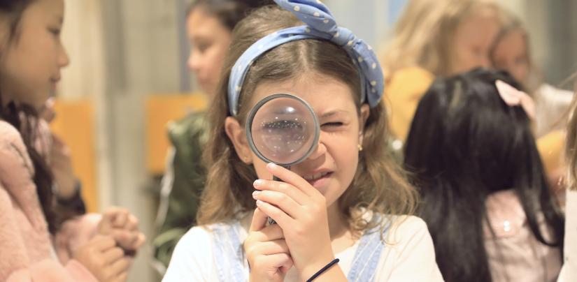 Young girl holding 3D printed magnifying glass with other girls in background