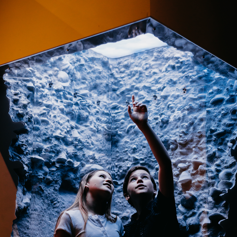 Two children standing inside a simulated archeological trench, the replicated surfaces of which were printed by ProtoSpace