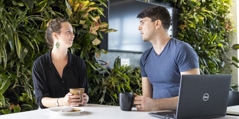 Two young people sit talking and drinking tea