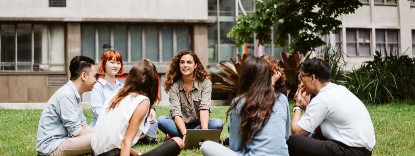 Group of diverse students sitting in a circle on the Alumni Green, smiling and chatting
