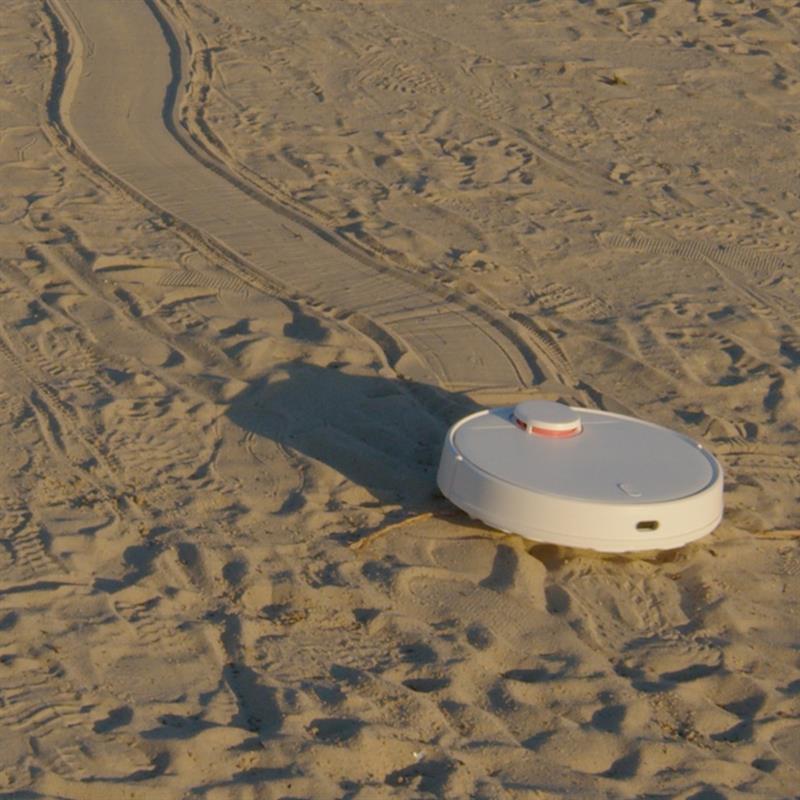 Image of a robot vacuum cleaner wandering across a beach. 