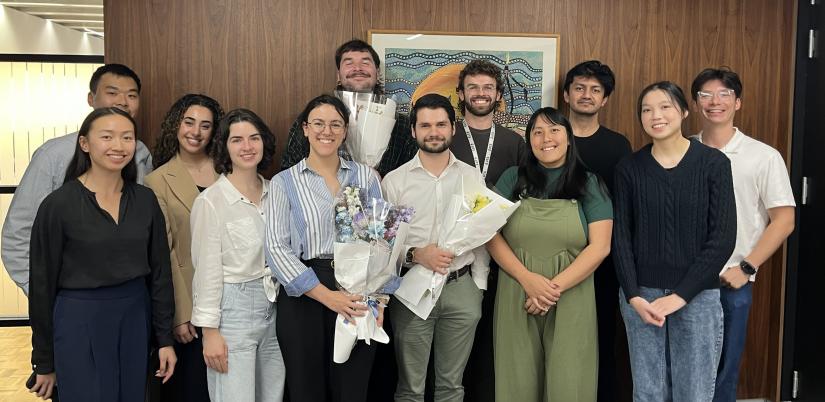 a group of young UTS graduates of Asian and Caucasian appearance stand in front of a wooden wall