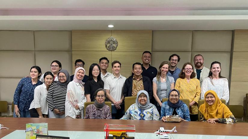 Members of the EMISI research team stand in three rows behind a desk. There are around 25 people.
