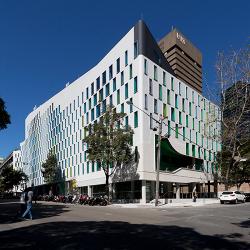 A building made from white concrete with curved, wave-like walls and green and blue window features