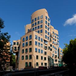 A brown brick building with multiple sections, curved features and large square windows