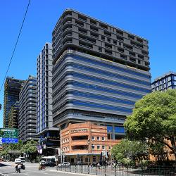 A large modernist commercial tower sits above the red brick facade of a heritage pub on Broadway
