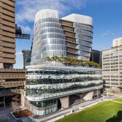 A glass-encased multi-level building with curved walls and an outdoor terrace filled with trees.