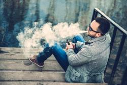 Overhead view of a man smoking an e-cigarette on a wharf at the edge of water