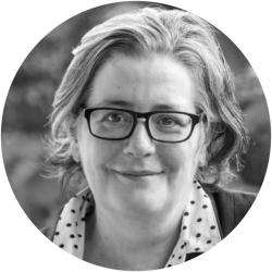 Round black and white photo of a woman with shoulder length hair wearing glasses looking at the camera