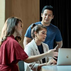 Three students talking around a laptop