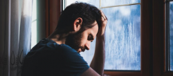 Man with head in hand leaning against a window