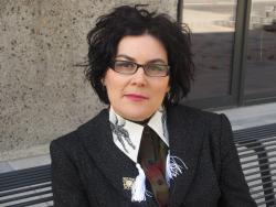 Woman smiling at camera. She has cropped short black hair and glasses.