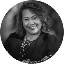 Round black and white photo of an indigenous woman smiling looking at the camera with arms folded