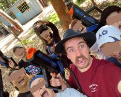 A young man and kids taking a fun group selfie holding water pistols.