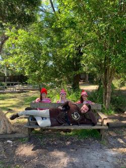 A young man sprawls across a park bench with three young women in Where's Wally costumes behind him.