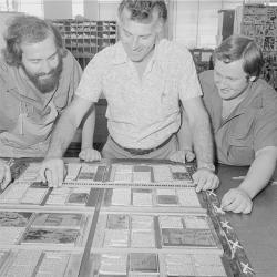 Black and white, three smiling men working on old printing press