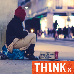 Person with a begging sign, sitting on a box, rugged up against the cold