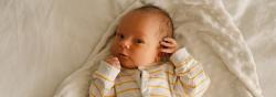 Baby in yellow and white jumpsuit lies on white blanket