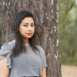 Woman standing in front of tree looking into camera.