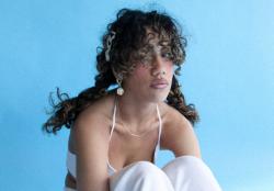 woman with curly hair wearing white sitting with knees up and her arms crossed under her knees