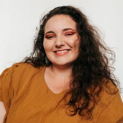 woman with long dark curly hair, burnt orange top, orange eye shadow, smiling at camera