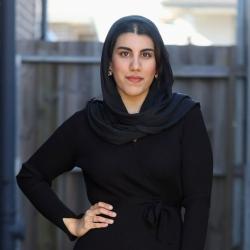 Woman dressed in black dress and hijab with hand on her hip.