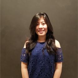 Woman with long hair wearing a blue blouse smiles into camera.