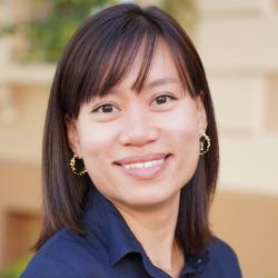 A woman wearing blue collard shirt smiles into the camera.